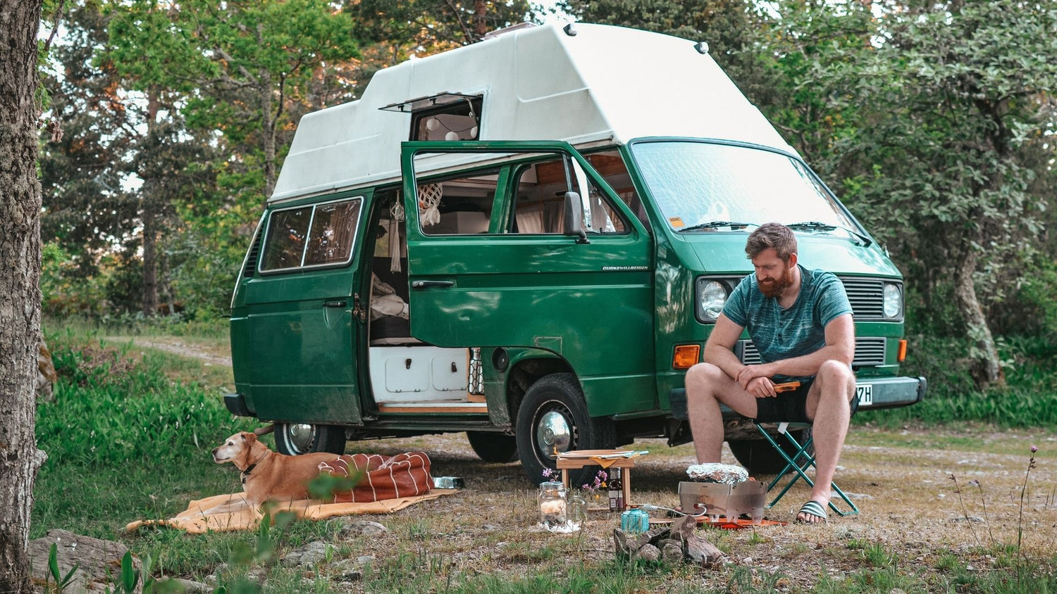 Junger Mann campt im Wald mit seinem Hund und grillt auf dem mobilen SKOTTI Grill